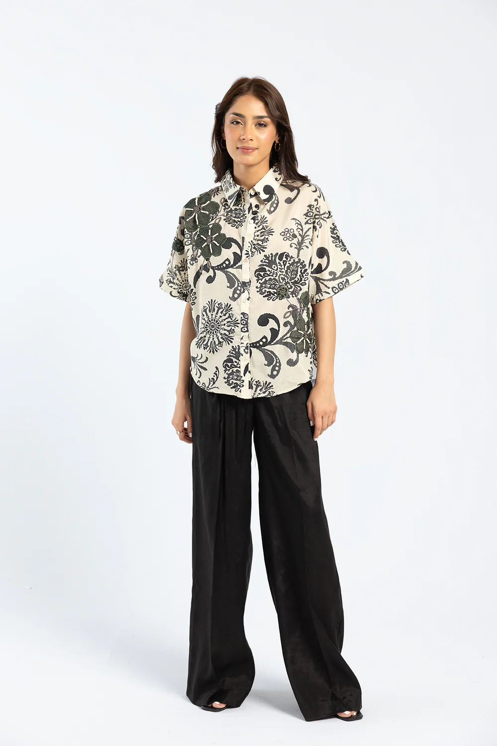 "Model wearing a beige button-down cotton shirt with black floral print and loose-fit black pants"